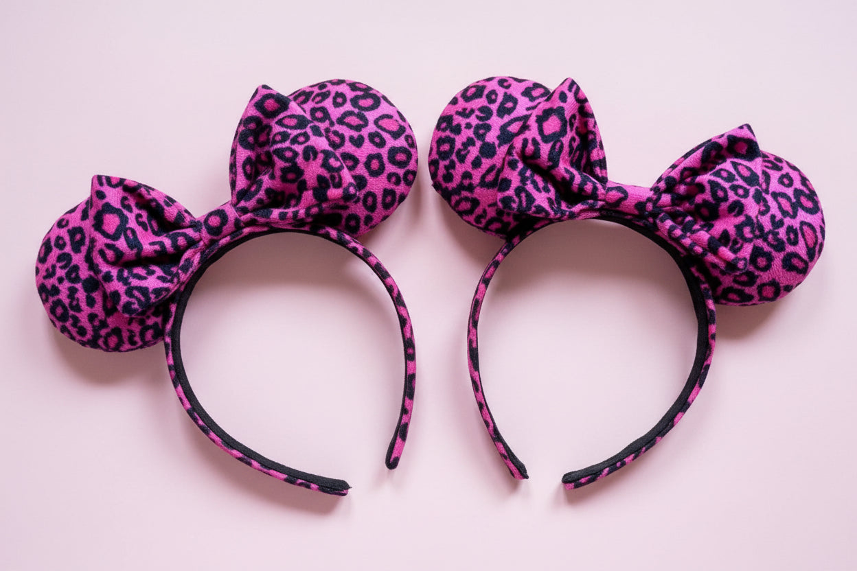 Two pink leopard print headbands with bows on a light pink background