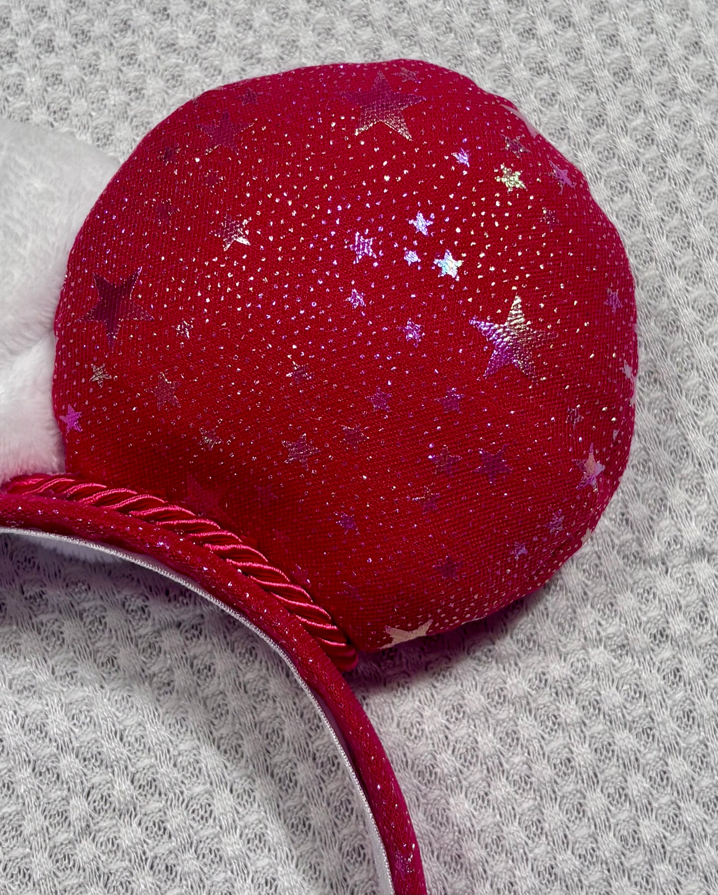 Handmade and ready to ship red mouse ears with iridescent stars on both the front and back along with the headband as well. The set has a white soft bow. Item is shown on a white background.