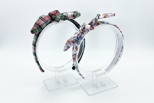 Made and ready to ship. Two handmade and ready to ship headbands with twisted bows on the top of the headbands on a clear stand against a white background