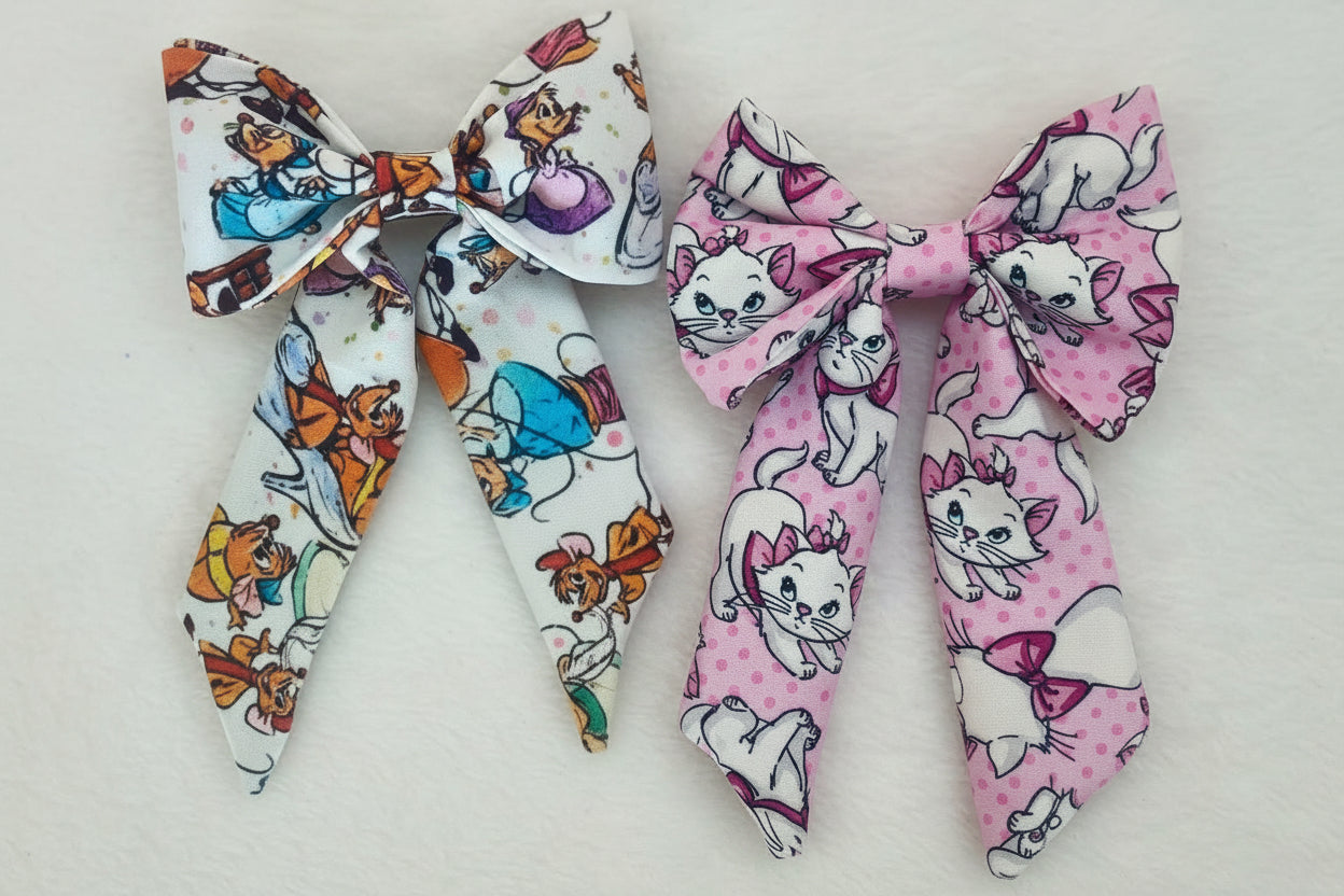 Two fabric bows with character prints of Cinderella sewing mice on one and Marie from The Aristocats on the other bow shown on a glittery orange background