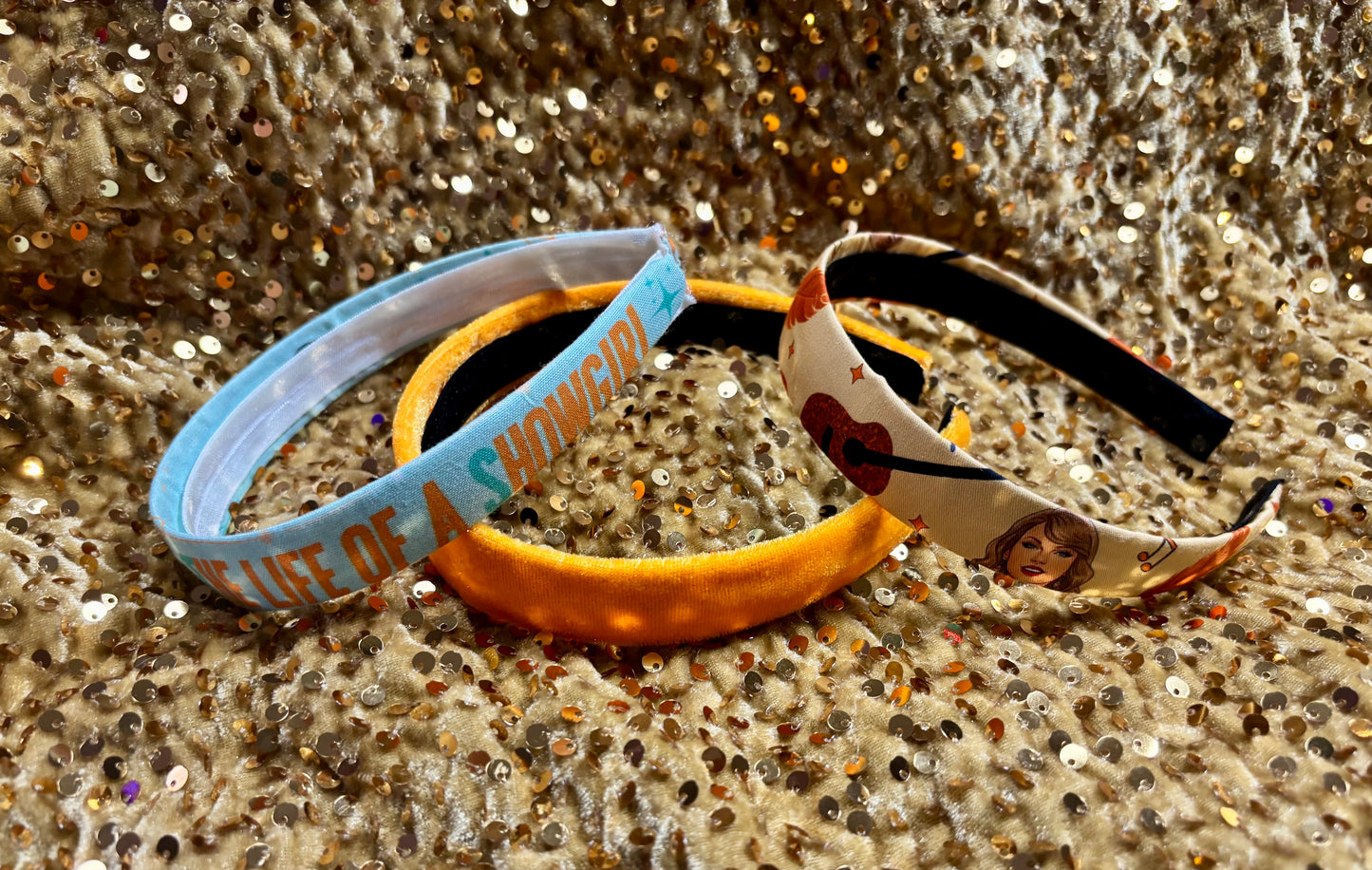 Three Showgirl themed headbands on a glittery surface
