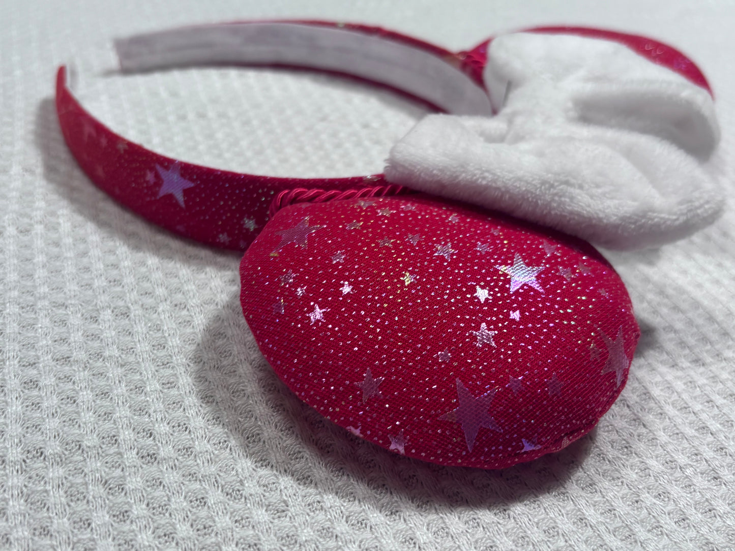 Handmade and ready to ship red mouse ears with iridescent stars on both the front and back along with the headband as well. The set has a white soft bow. Item is shown on a white background.