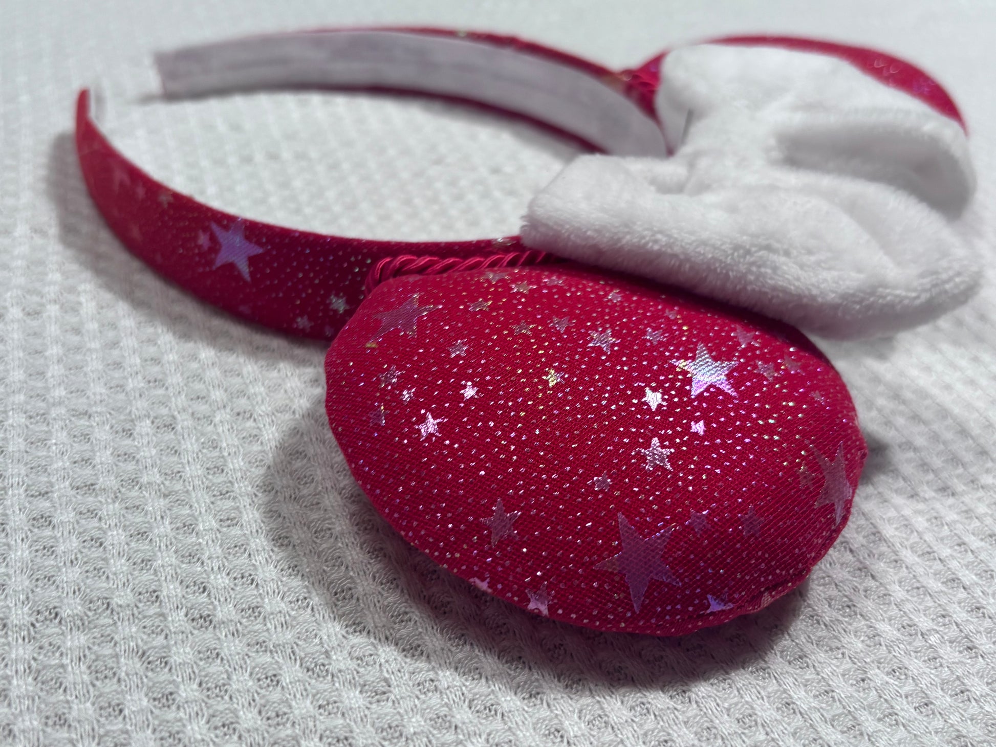 Handmade and ready to ship red mouse ears with iridescent stars on both the front and back along with the headband as well. The set has a white soft bow. Item is shown on a white background.