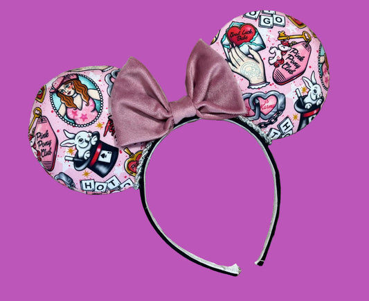 A set of ear headband accessories featuring a pink and white illustrated pattern with a dusty pink velvet bow in the center, displayed on a pink background.