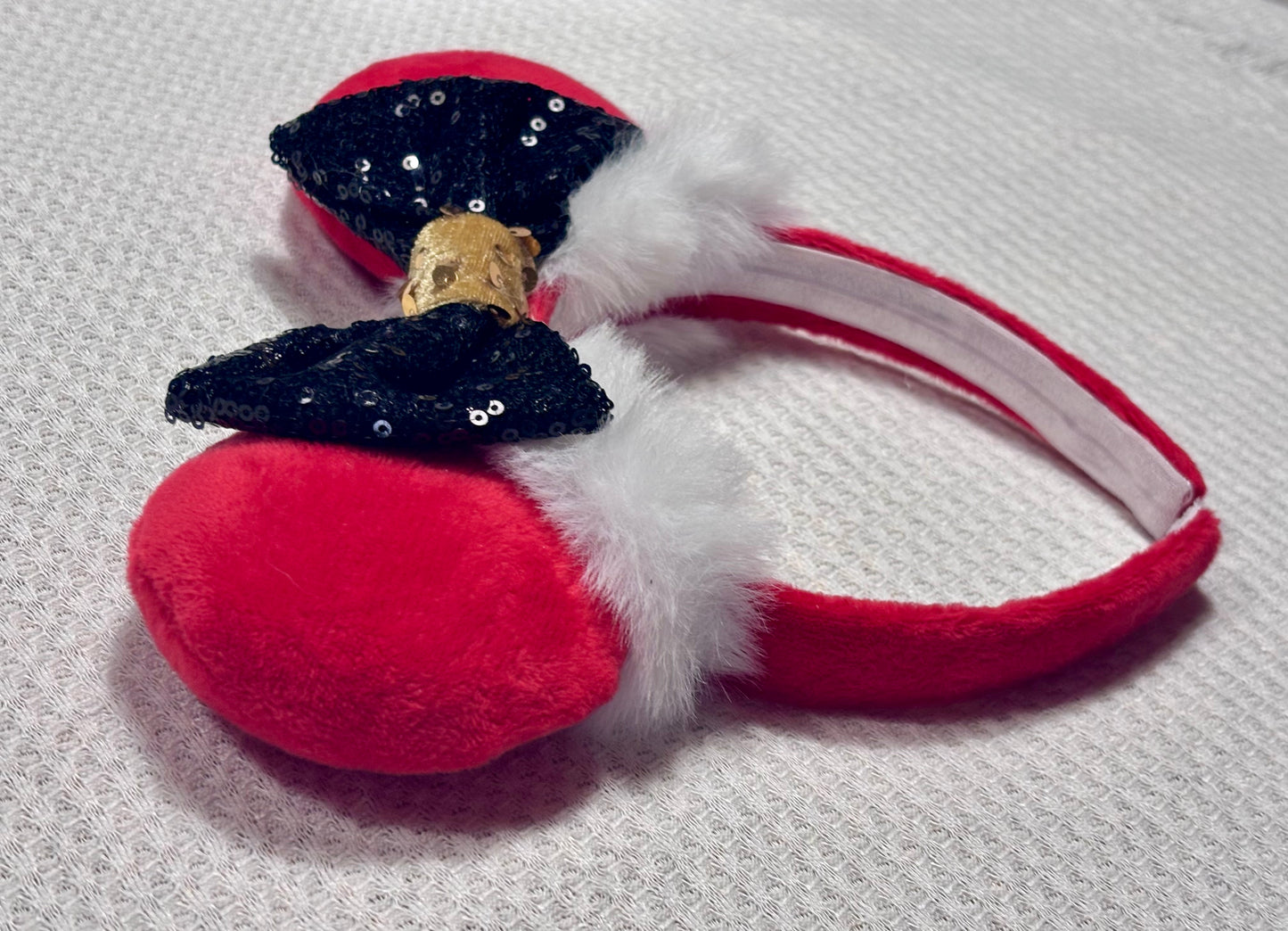 Minnie Mouse ears headband with red plush ears and black bow with gold middle and fluffy white trim on a white background