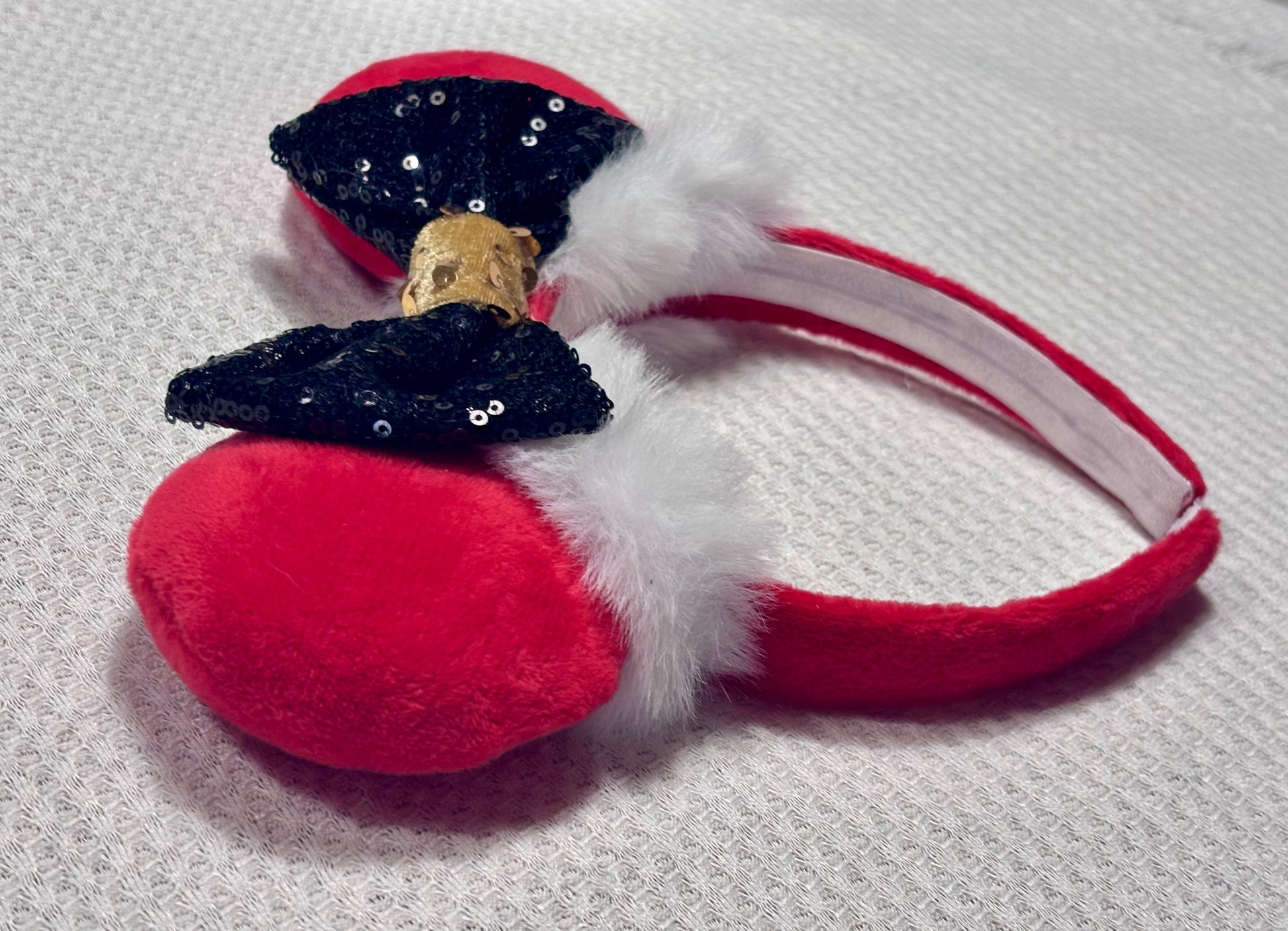 Minnie Mouse ears headband with red plush ears and black bow with gold middle and fluffy white trim on a white background