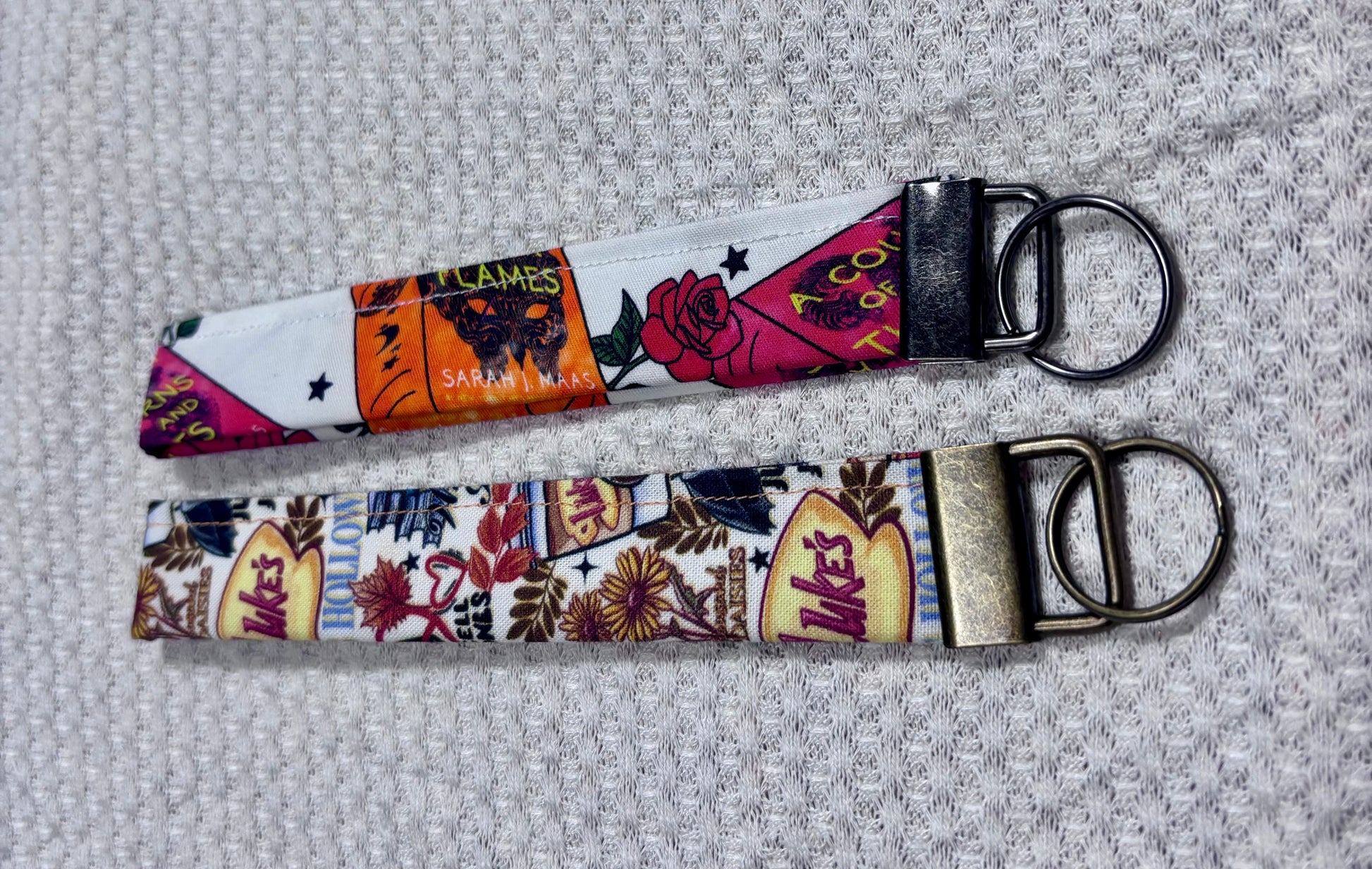 Two colorful keychains with ACOTAR and Gilmore Girls inpired patterns on a textured gray background.