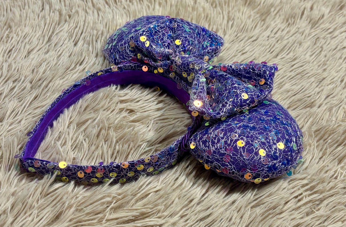 A purple iridescent sequined headband with two large mouse shaped ears. Side view of the headband.