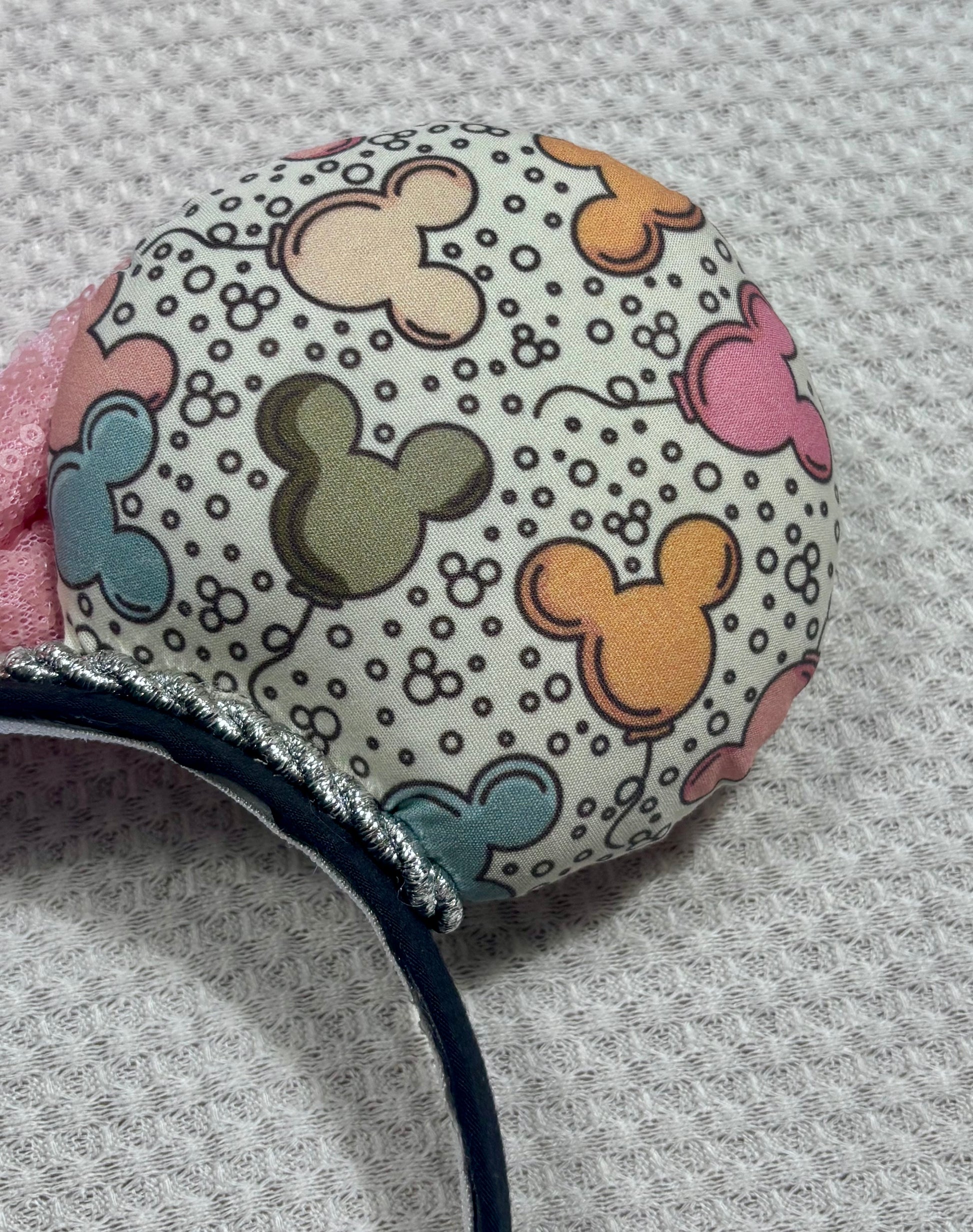 Close up of back right mouse ear. Handmade and ready to ship Mouse ears with mouse balloon fabric with a light pink sequin bow. Perfect for Main Street. Shown on a white background.