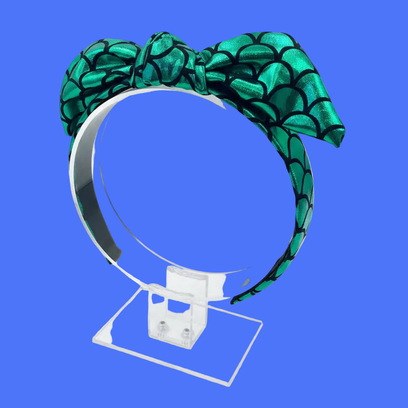 Green mermaid scales headband with bow on a clear stand. Made and ready to ship.