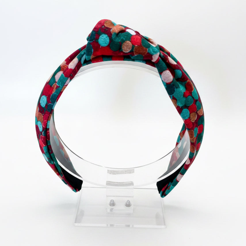 Colorful Christmas colors patterned headband on a clear stand against a white background.