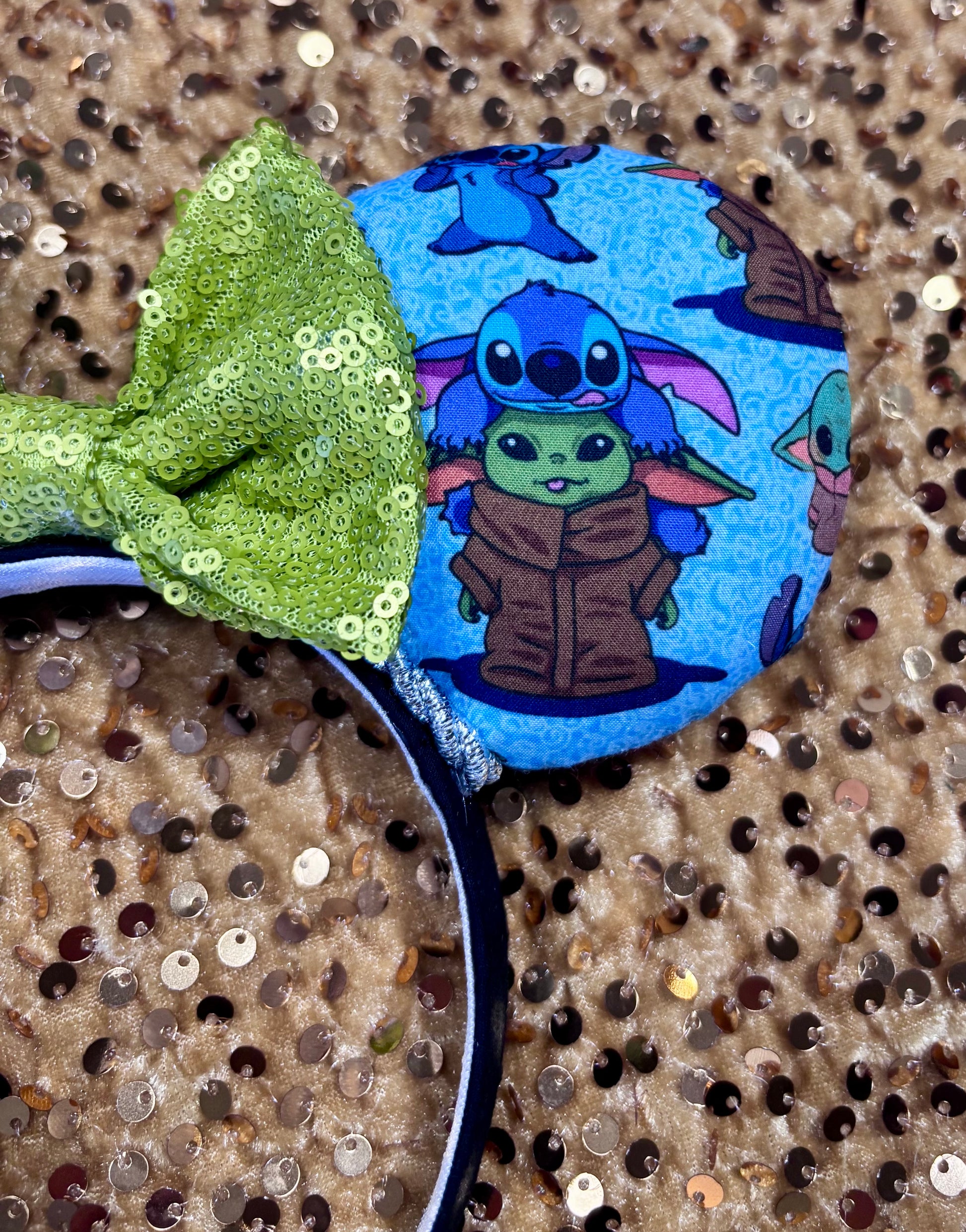 Close up of Stitch and Baby Yoda on front of mouse ear. Handmade and ready to ship small friend aka Stitch and Baby Yoda Mouse ears with a lime green sequin bow. Of course, you can request any bow in sequin if you prefer and I will attach it. Shown on a white background.