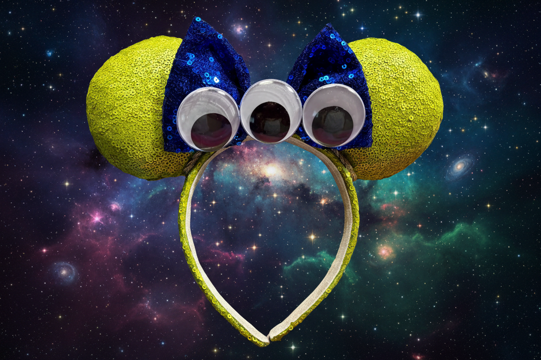 Lime green mouse ears and headband with blue sequin bow and three googly eyes and twisted trim. Shown against a starry space background
