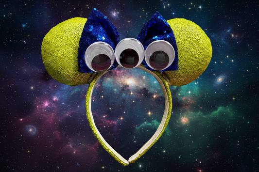 Lime green mouse ears and headband with blue sequin bow and three googly eyes and twisted trim. Shown against a starry space background