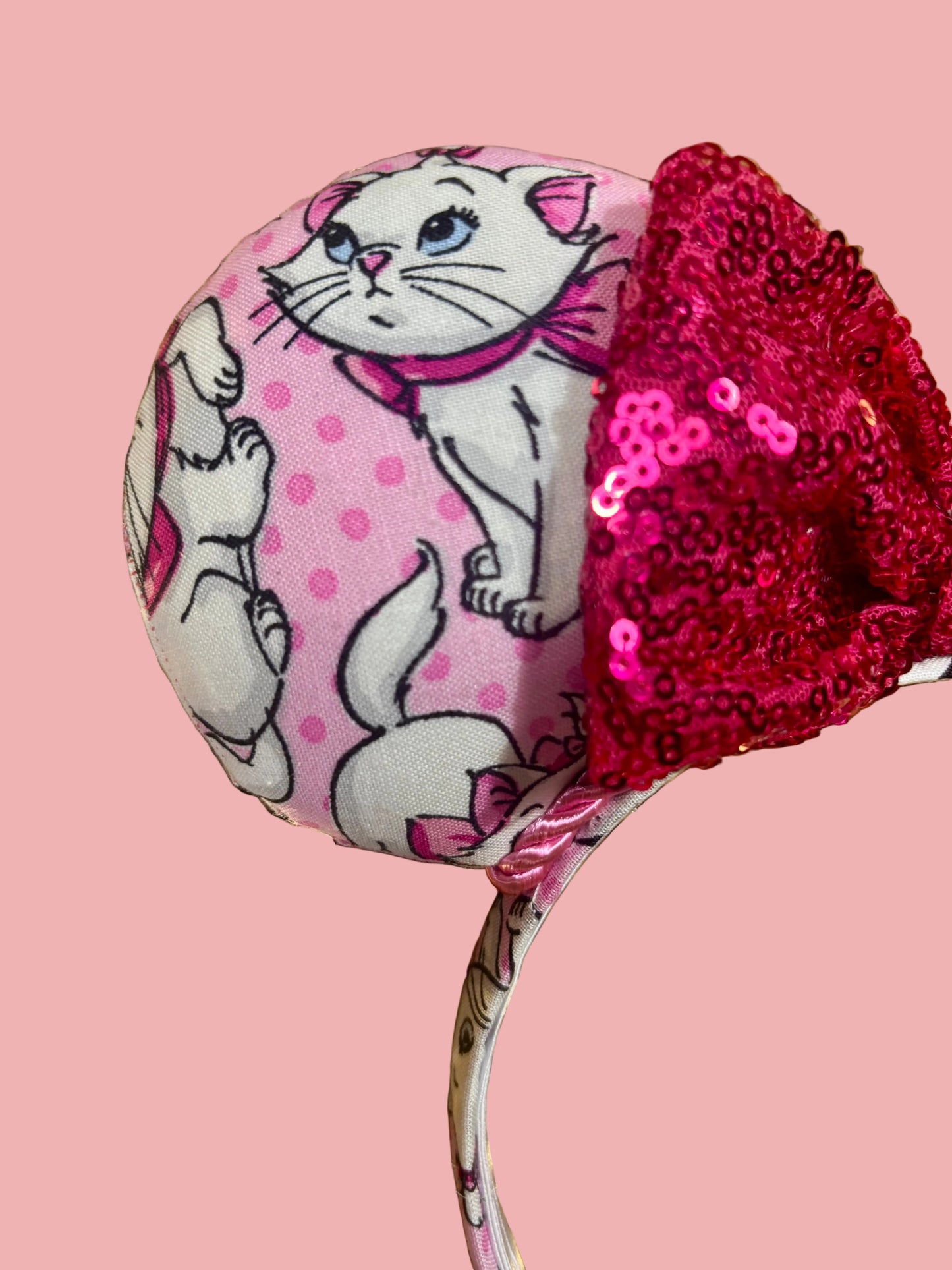 Close up of front mouse ear and the hot pink bow. Handmade and ready to ship Marie Inspired Mouse ears with images of her on the front and back of mouse ears shown with a Hot Pink sequin bow option. The headband has a matching Marie poly cotton fabric and is a universal sized headband. 
