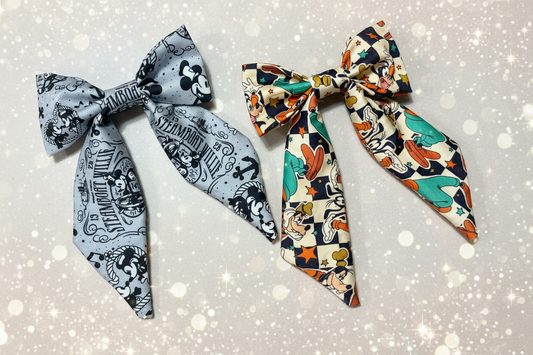 Two hair bows, one is steamboat Willie themed and the other is a checkered goofy bow shown on a light background