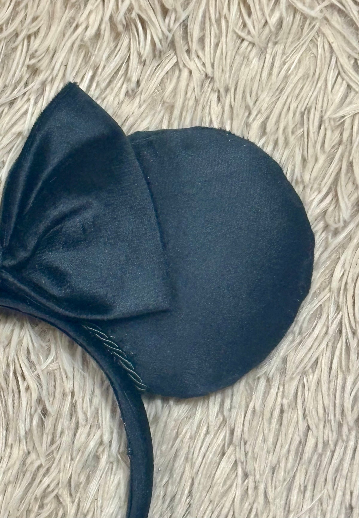A close-up of a black velvet mouse-ear headband with a large bow, laid on a textured beige shag rug.