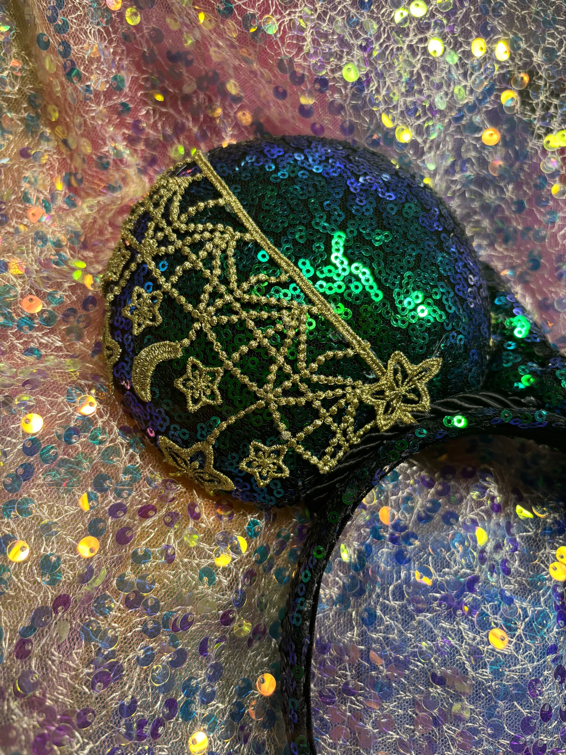 Mouse Ear headband that is a Handmade Iridescent blue and green sequins with gold sun, moon and stars attached to them. bow with star and moon patterns on a glittery background.