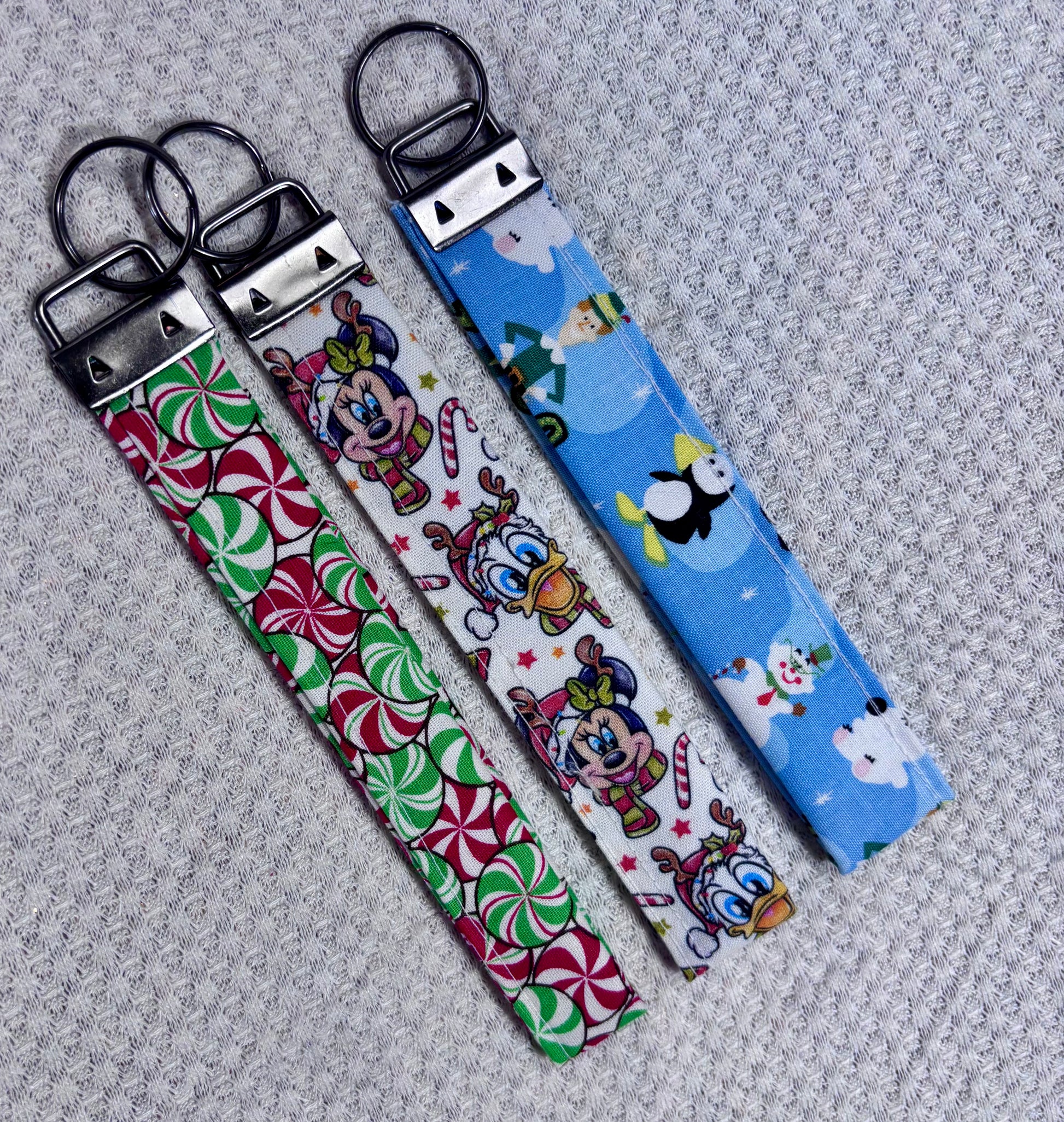 Three fabric keychains with cartoon character designs on a textured gray surface.