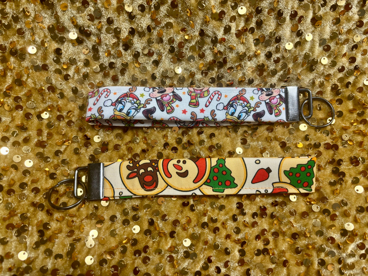 Two keychains with festive designs on a glittery gold background