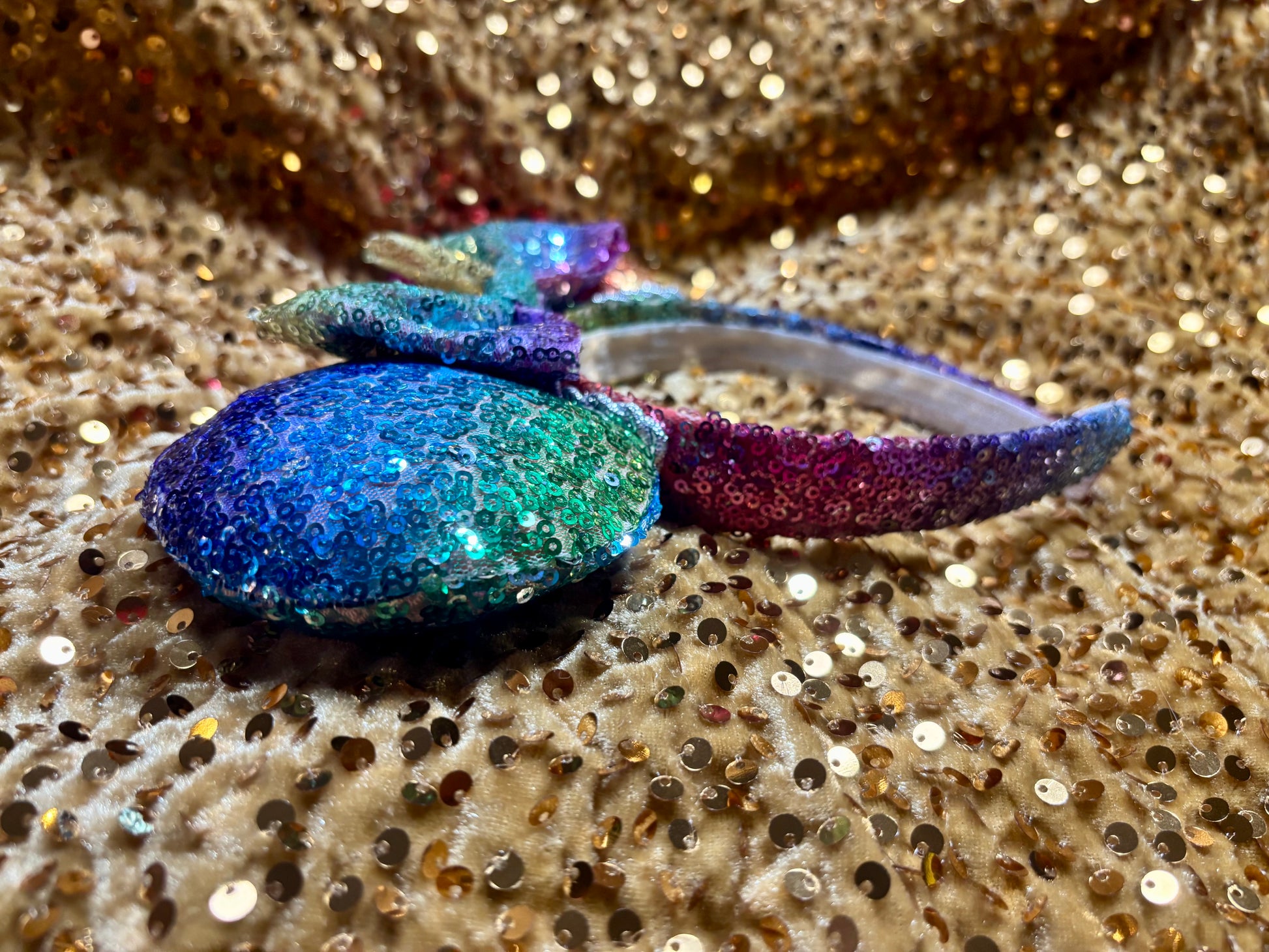 Handmade and ready to ship. Mouse ears with rainbow fabric are on the front and back of mouse ears along with the headband with a matching rainbow sequin bow. Shown on a gold sequin background.