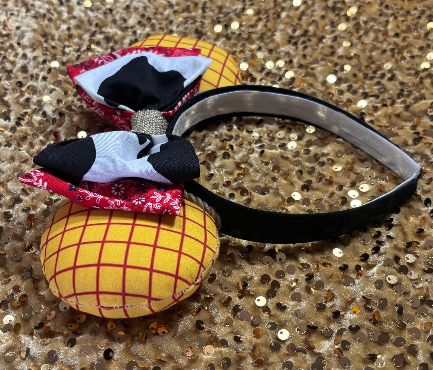 Handmade and ready to ship. Sheriff Woody Inspired mouse ears with the fabric on both the front and back that looks like his shirt. The fabric on the headband is black and is universal sized and fits most. The set has a bandana and cow print layered bow with brown trim along the inner ears to look like rope. Item is shown on a white background.