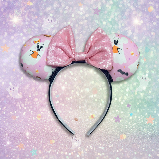 An ear headband featuring a pink sequined bow in the center and pink ghost-patterned ears.