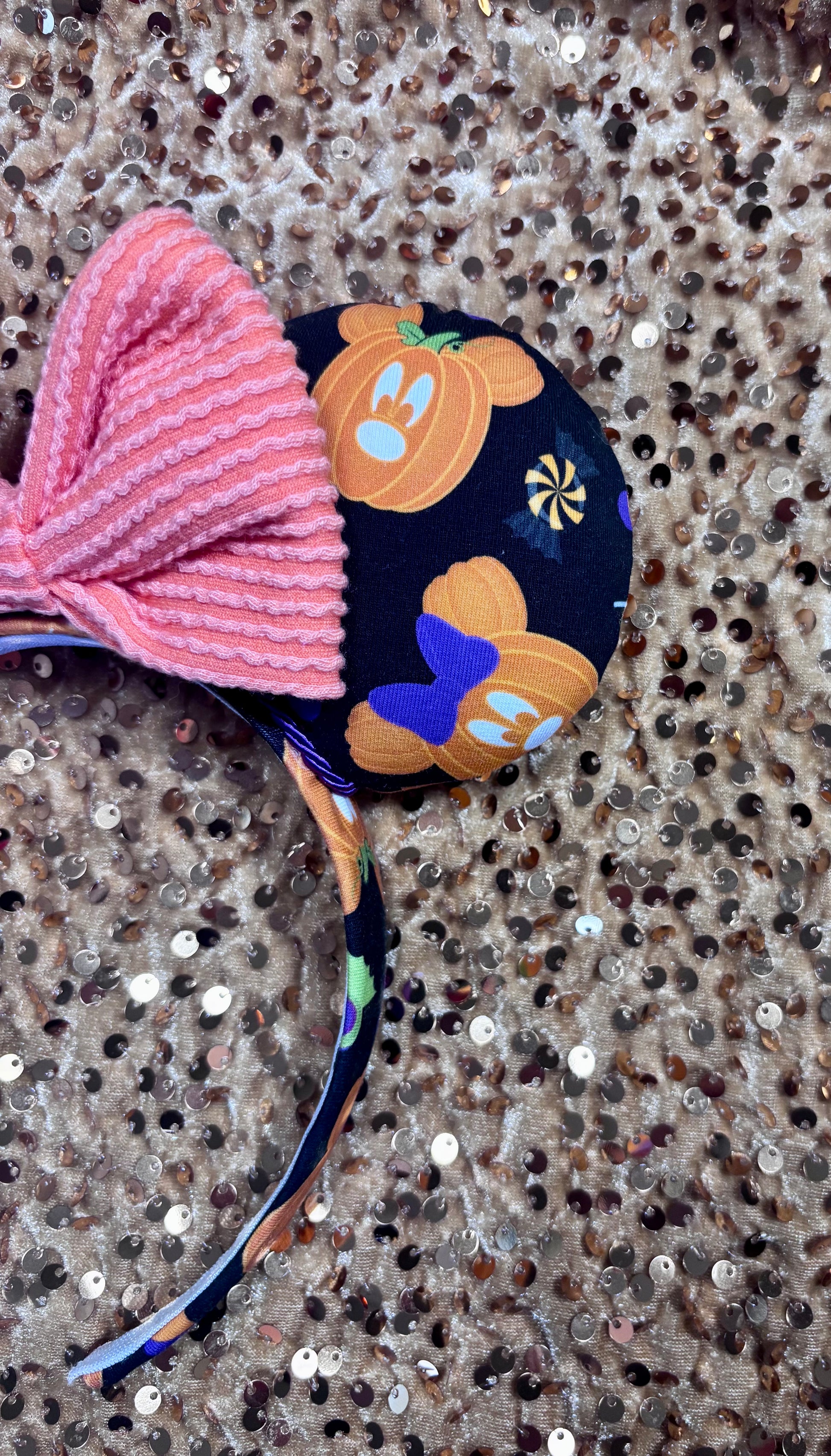 Halloween-themed headband with bow on a textured surface. Showing the front left mouse ear.