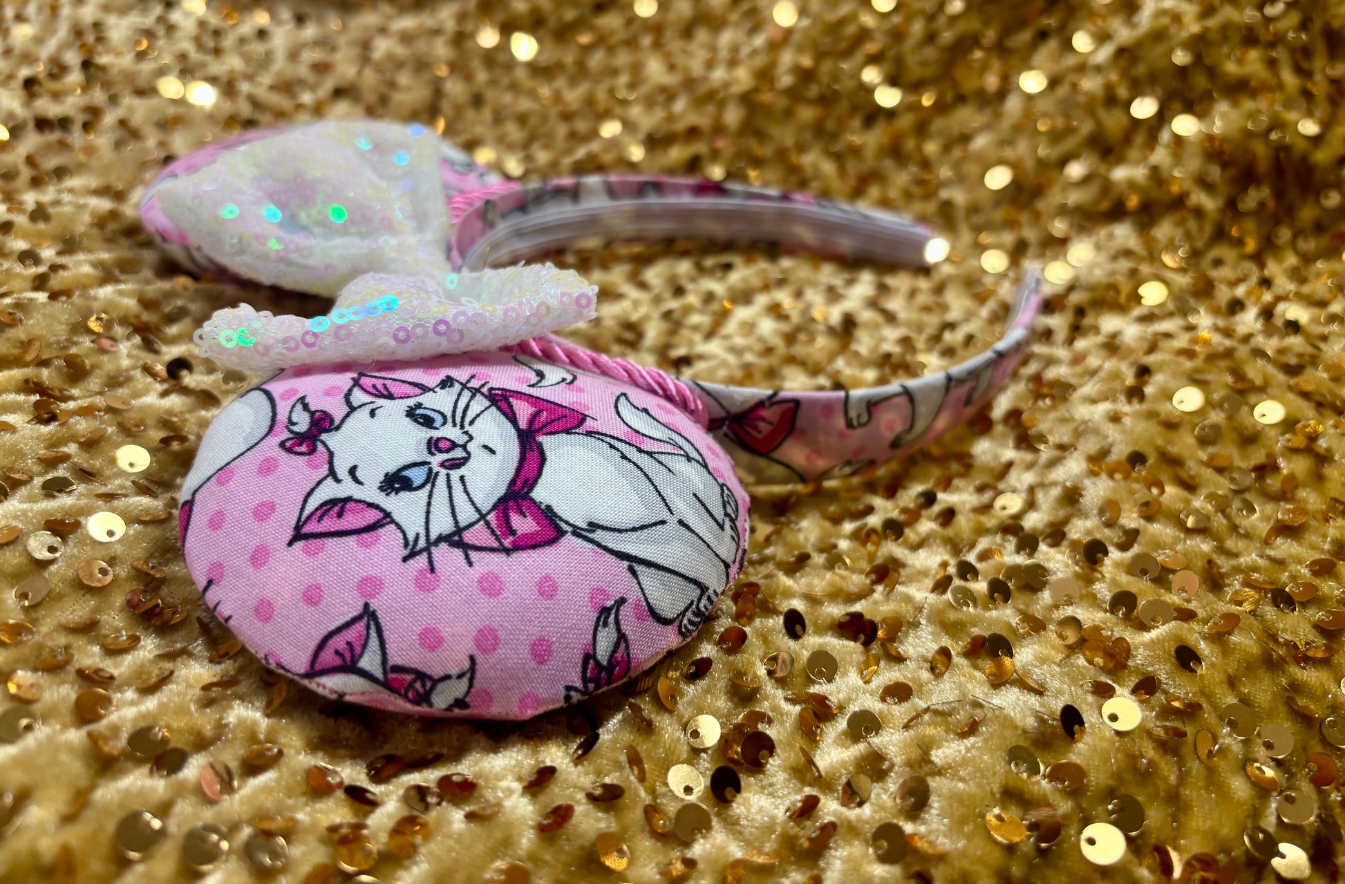 Pink mouse ear headband with white bow shown on a gold glitter background