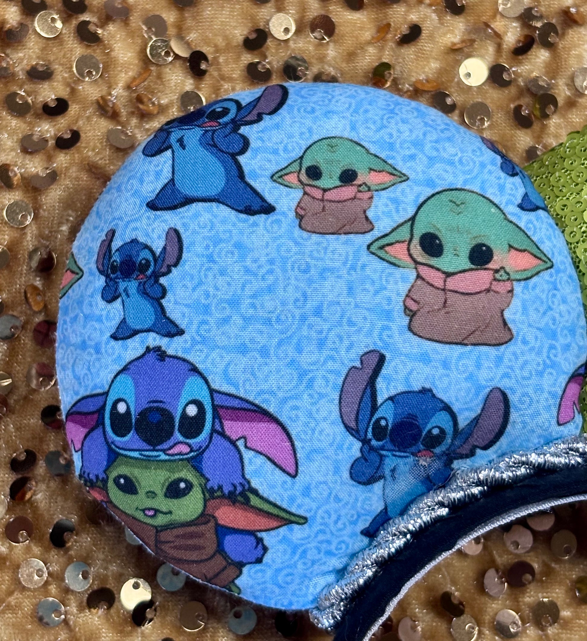 Back side of left mouse ear close up showing stitches and baby Yoda's on the fabric. Handmade and ready to ship small friend aka Stitch and Baby Yoda Mouse ears with a lime green sequin bow. Of course, you can request any bow in sequin if you prefer and I will attach it. Shown on a white background.