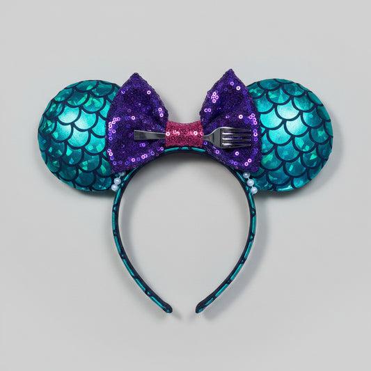 Mermaid-themed headband with teal scales and a purple sequin bow with a red middle and a dinglehopper middle piece. Pearl garland trim along inner ears m on a matching mermaid scales headband.
