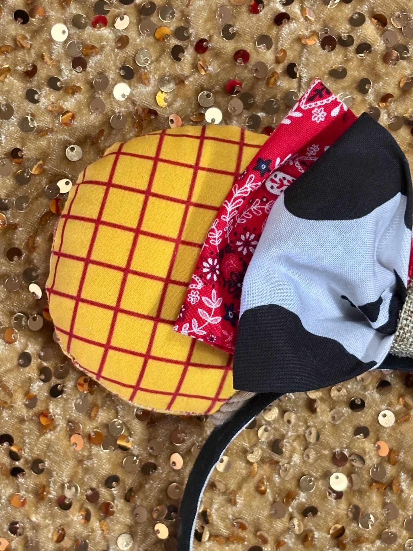 Handmade and ready to ship. Sheriff Woody Inspired mouse ears with the fabric on both the front and back that looks like his shirt. The fabric on the headband is black and is universal sized and fits most. The set has a bandana and cow print layered bow with brown trim along the inner ears to look like rope. 