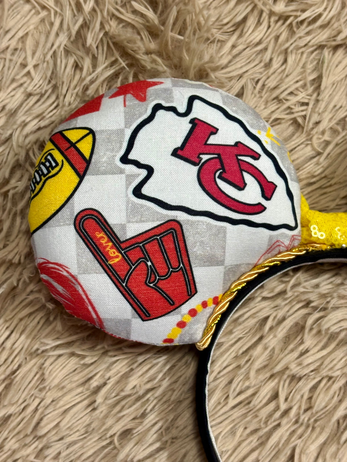 An ear headband featuring a bright yellow sequined bow. The set has TS and Chiefs images on it. Set on a universal sized headband.