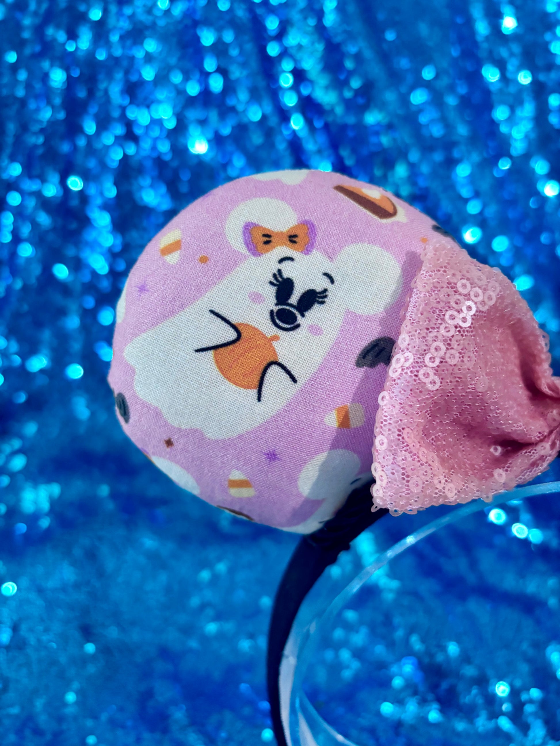 Front mouse ear view of fabric and mouse shaped ghost. Handmade and ready to ship Halloween Pink Ghosts Mouse ears with the fabric with mouse shaped ghosts on pink fabric is on the ears, front and back and a light pink sequin bow. The headband is a universal sized headband and has black poly cotton fabric on it.