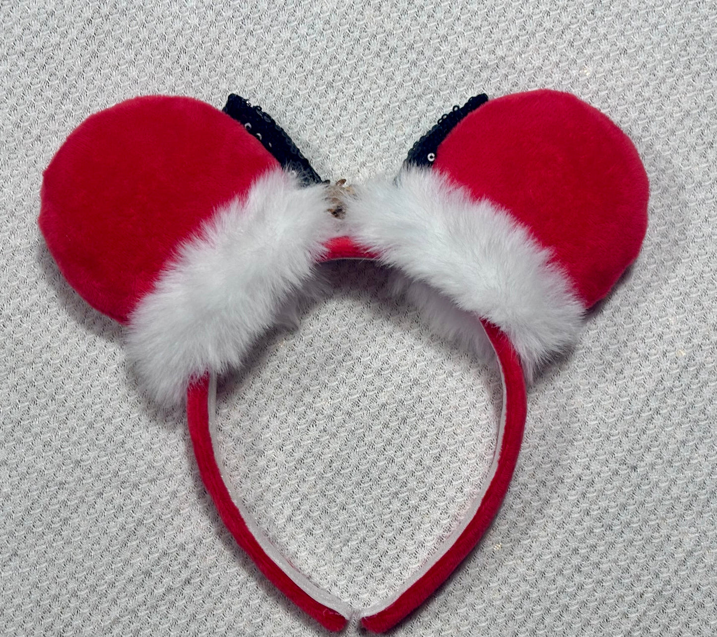 Minnie Mouse ears headband with red plush ears and black bow with gold middle and fluffy white trim on a white background