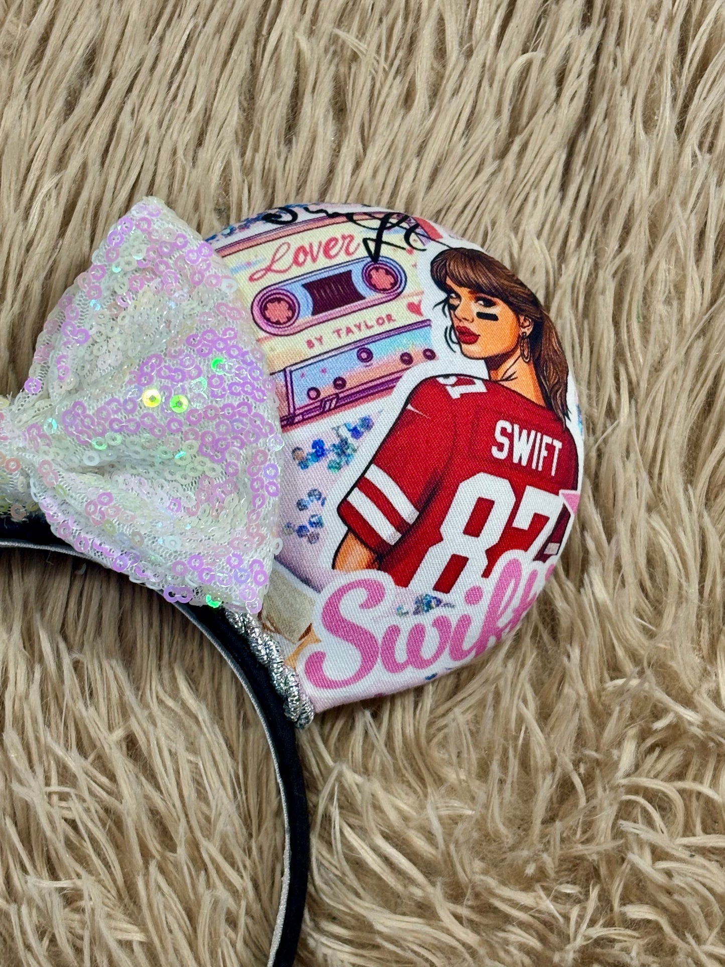 An ear headband with a large iridescent bow and custom printed ears featuring retro cassette graphics, a pink star, and a portrait of singer.