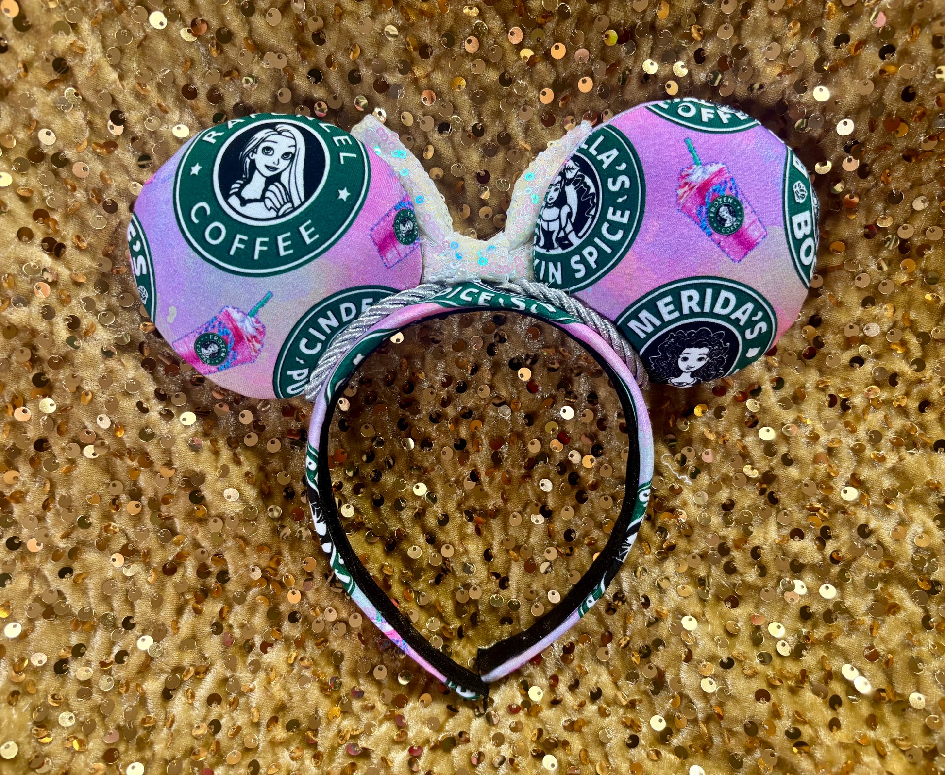 Back view of mouse ears. Handmade and ready to ship custom ears with popular coffee themed with princesses on fabric. Shown on a gold sequin background.