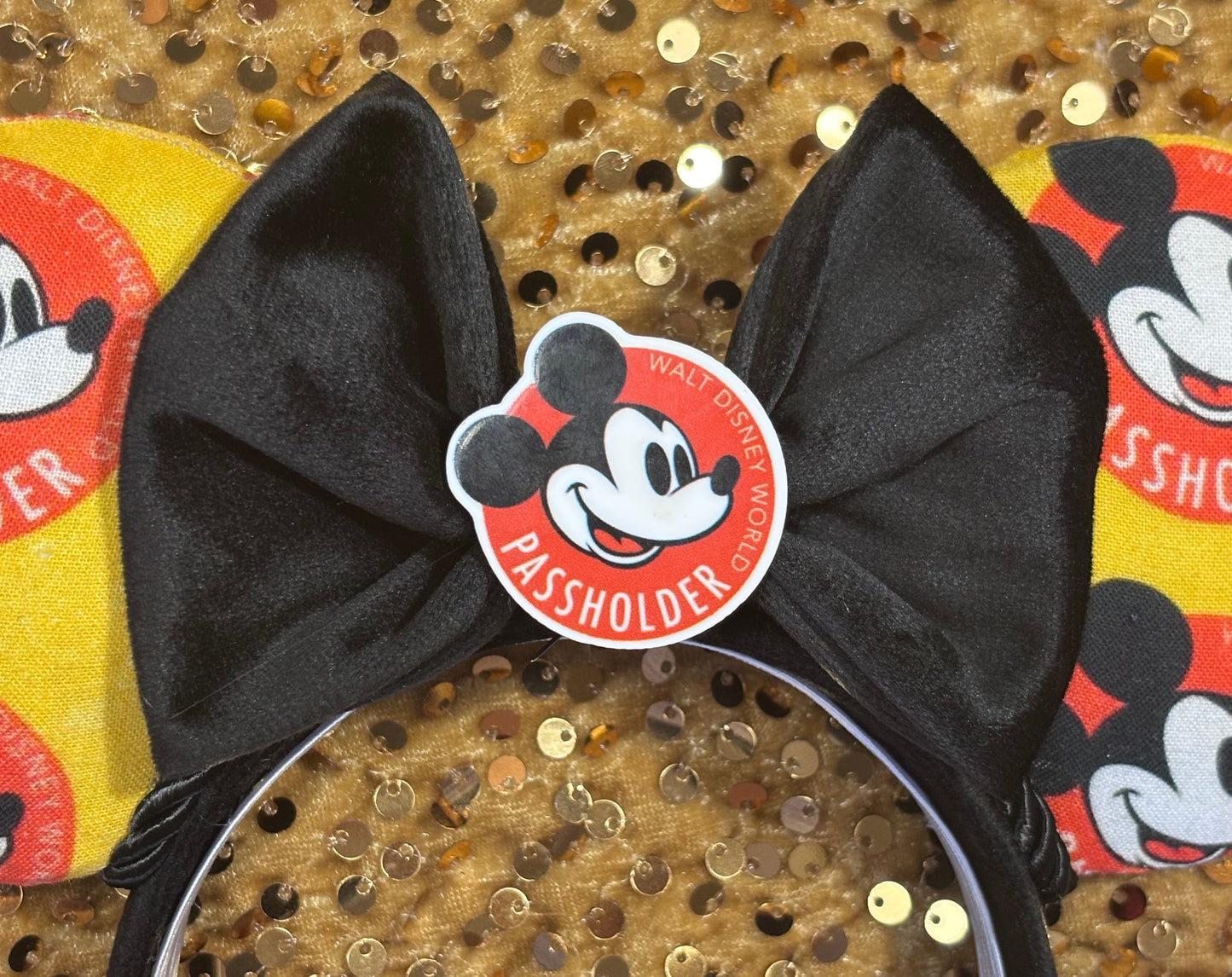 Black velvet bow on middle of headband with a passholder flatback shown on a sequined background