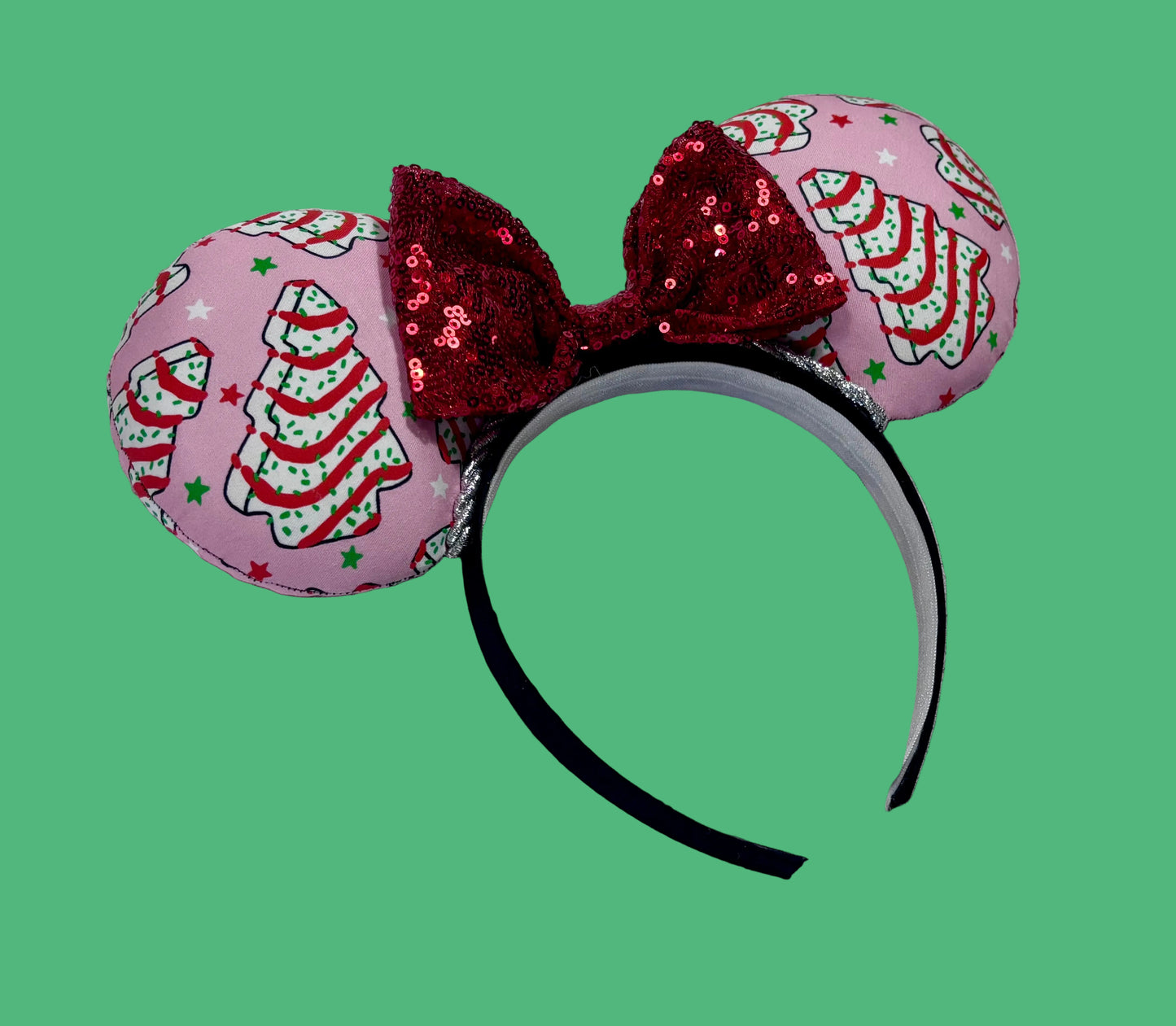 Angled view of the set. Handmade and ready to ship. Christmas cake fabric is on the ears front and back with a silver twisted trim. the bow is a red sequin one and the headband is a black poly cotton band that is universal.