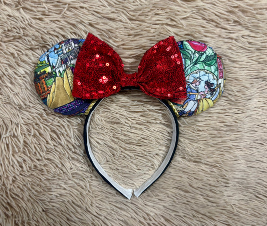 A pair of ears headband featuring a vibrant red sequined bow in the center and patterned fabric ears with colorful stained-glass style illustrations, displayed on a beige faux fur background.