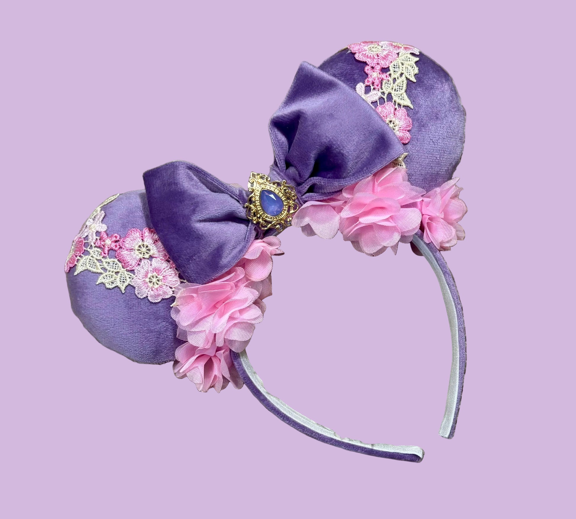 Purple and pink fabric mouse ears headband with a large velvet bow, floral lace appliques, and a purple gem accent.