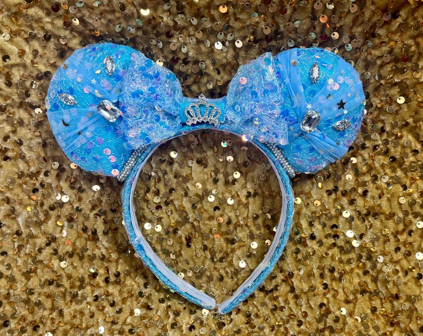 Blue glittery bow headband with tulle and silver embellishments on them and a rhinestone trim with a crown on the mouse ears bow. 