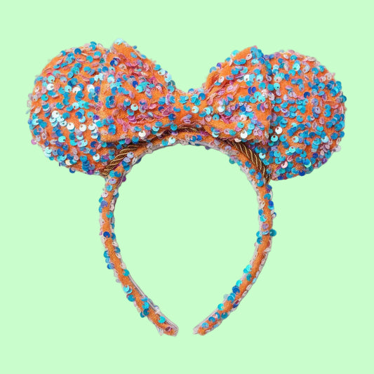 Sequined bow headband with orange and blue colors on a mint green background