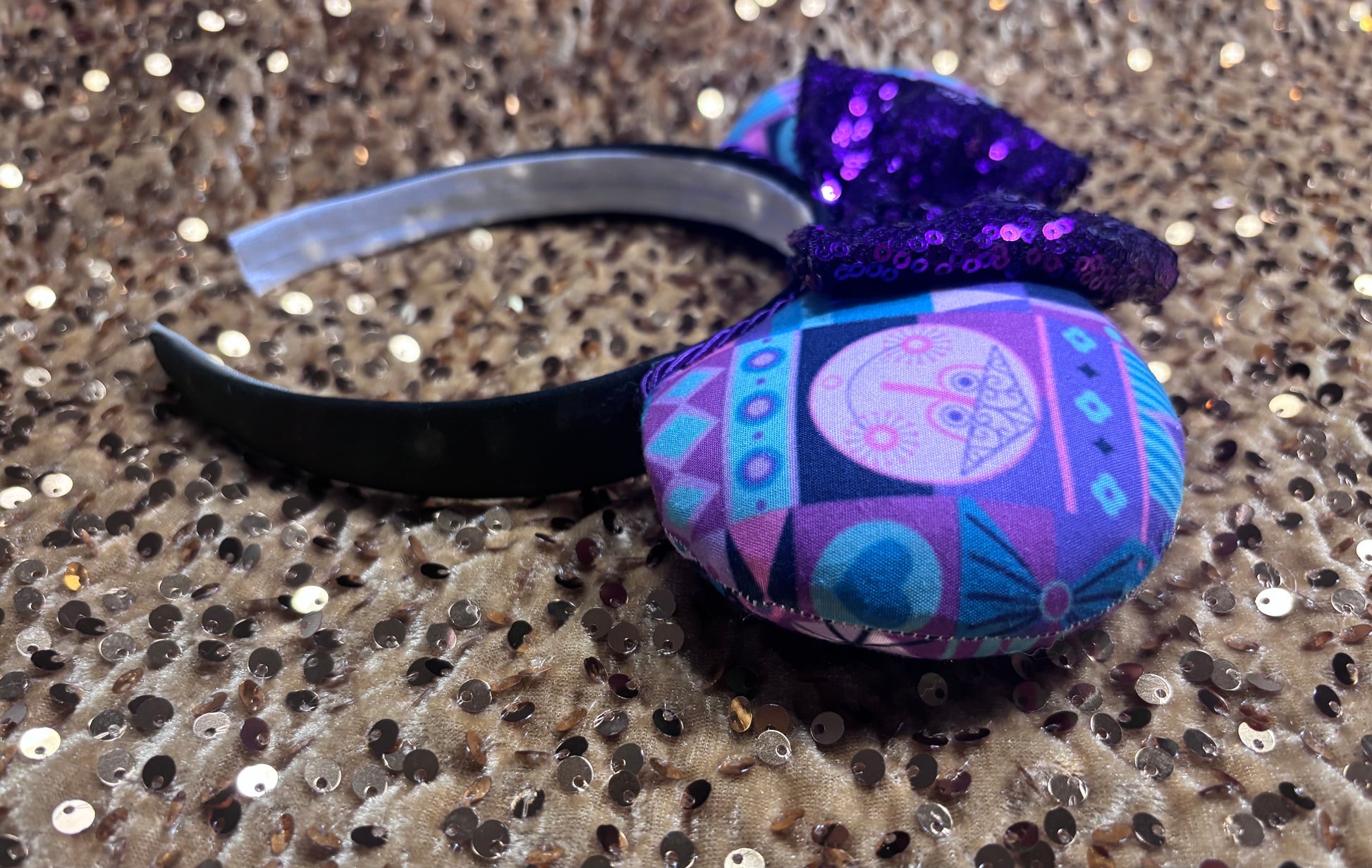 Colorful headband with a purple bow and geometric pattern on a glittery surface