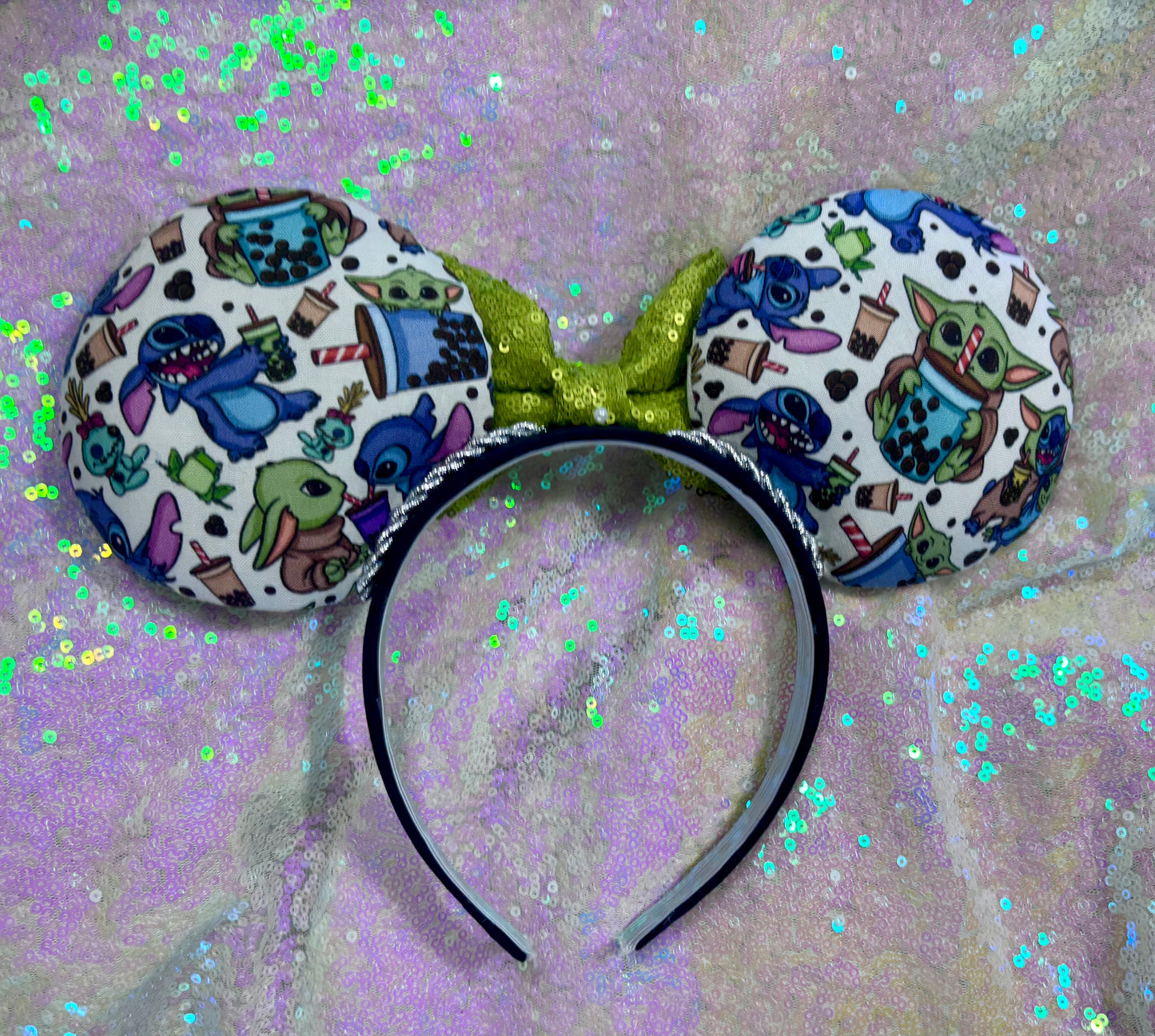 Handmade and ready to ship. Stitch and Baby Yoda are drinking coffee on the front and back with a lime green sequin bow. Shown on a white glitter background.