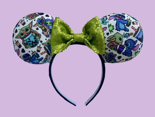 Handmade and ready to ship. Stitch and Baby Yoda are drinking coffee on the front and back with a lime green sequin bow. Silver twisted trim along the inner ears and attached to a universal sized black poly cotton headband.