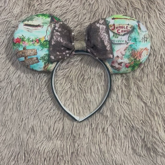 A pair of mouse ears headband featuring a colorful Jungle themed print on the ears and a dark brown sequined bow in the center.