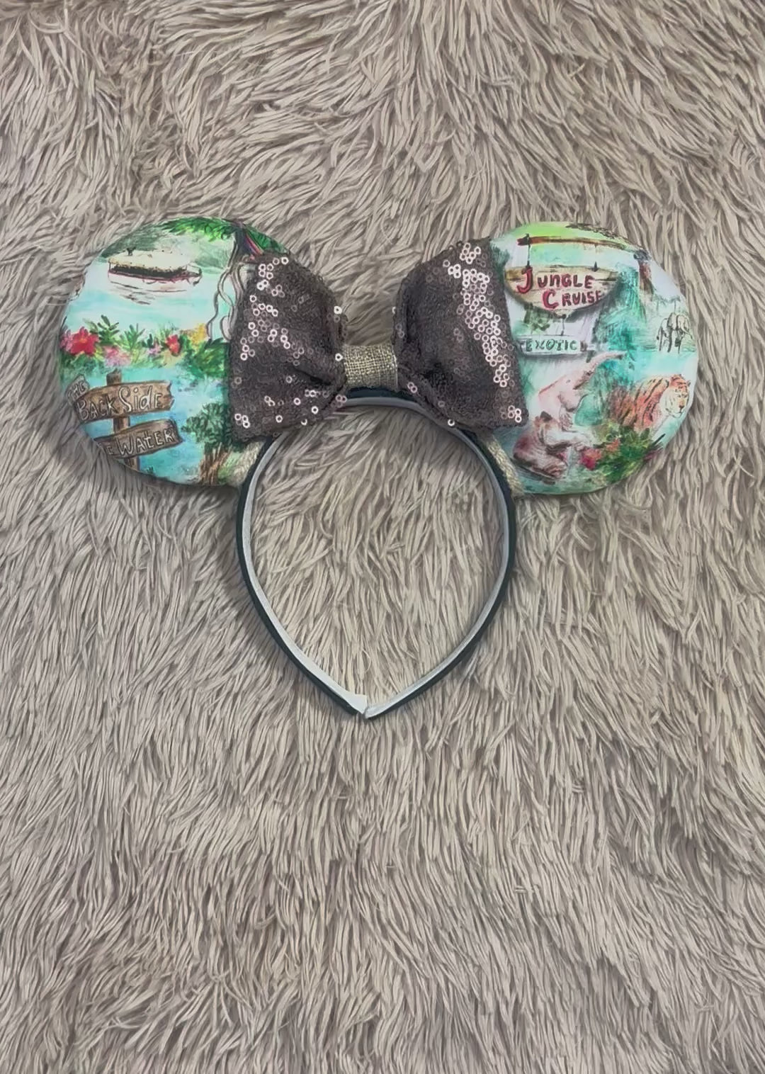 A pair of mouse ears headband featuring a colorful Jungle themed print on the ears and a dark brown sequined bow in the center.