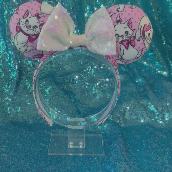 Handmade and ready to ship Marie Inspired Mouse ears with images of her on the front and back of mouse ears shown with a white iridescent sequin bow. The headband has a matching Marie poly cotton fabric and is a universal sized headband.