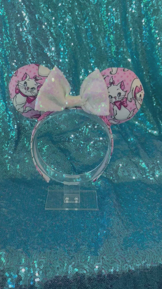 Handmade and ready to ship Marie Inspired Mouse ears with images of her on the front and back of mouse ears shown with a white iridescent sequin bow. The headband has a matching Marie poly cotton fabric and is a universal sized headband.